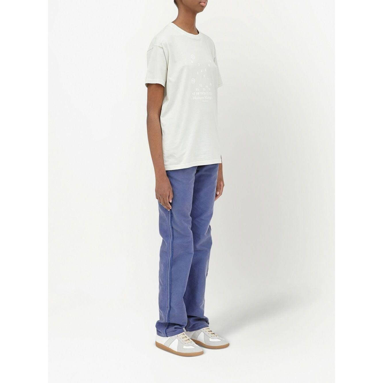 Model wearing Maison Margiela white logo-print crew-neck T-shirt with blue pants and sneakers, showcasing casual off-white cotton tee.