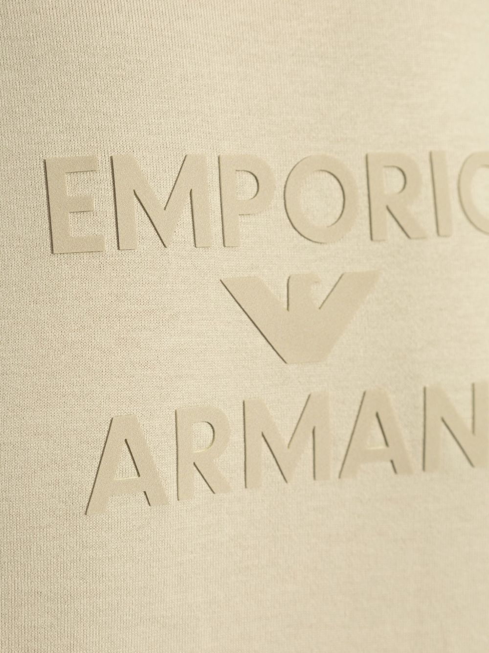 Beige Emporio Armani T-shirt with embossed logo design, showing a close-up of the front cotton fabric.