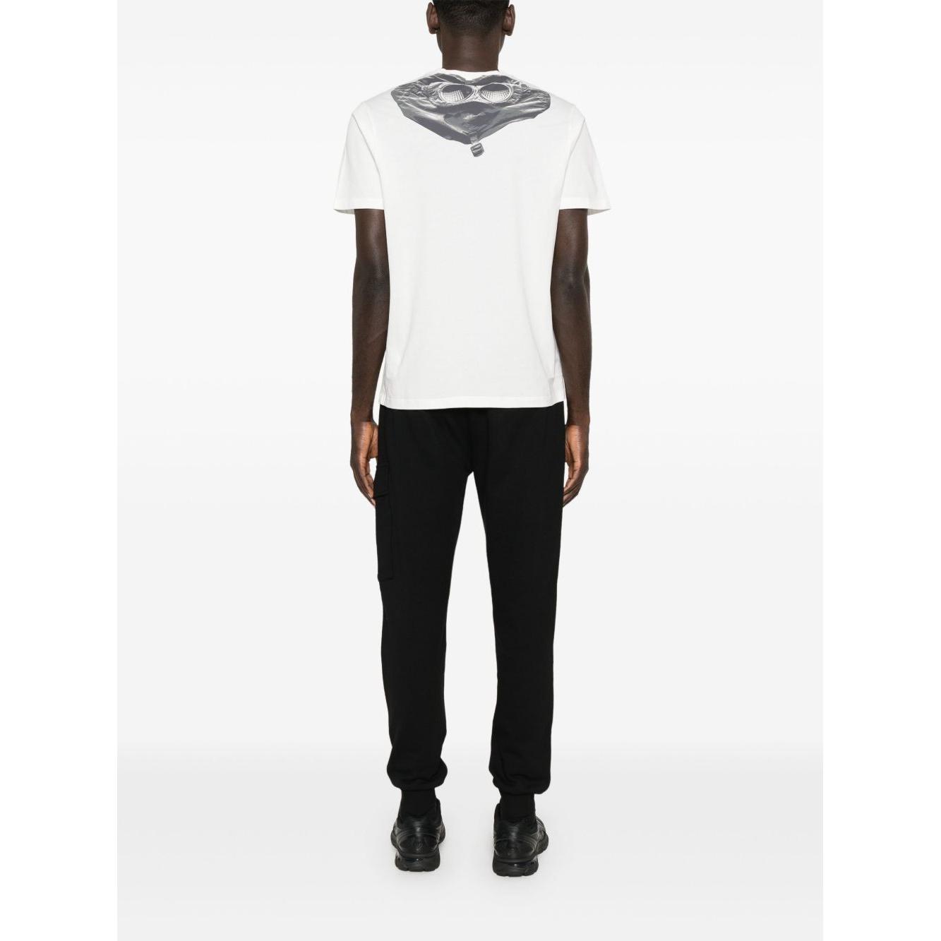 Back view of a man wearing a C.P. Company white T-shirt with signature Goggle print, paired with black pants and sneakers.