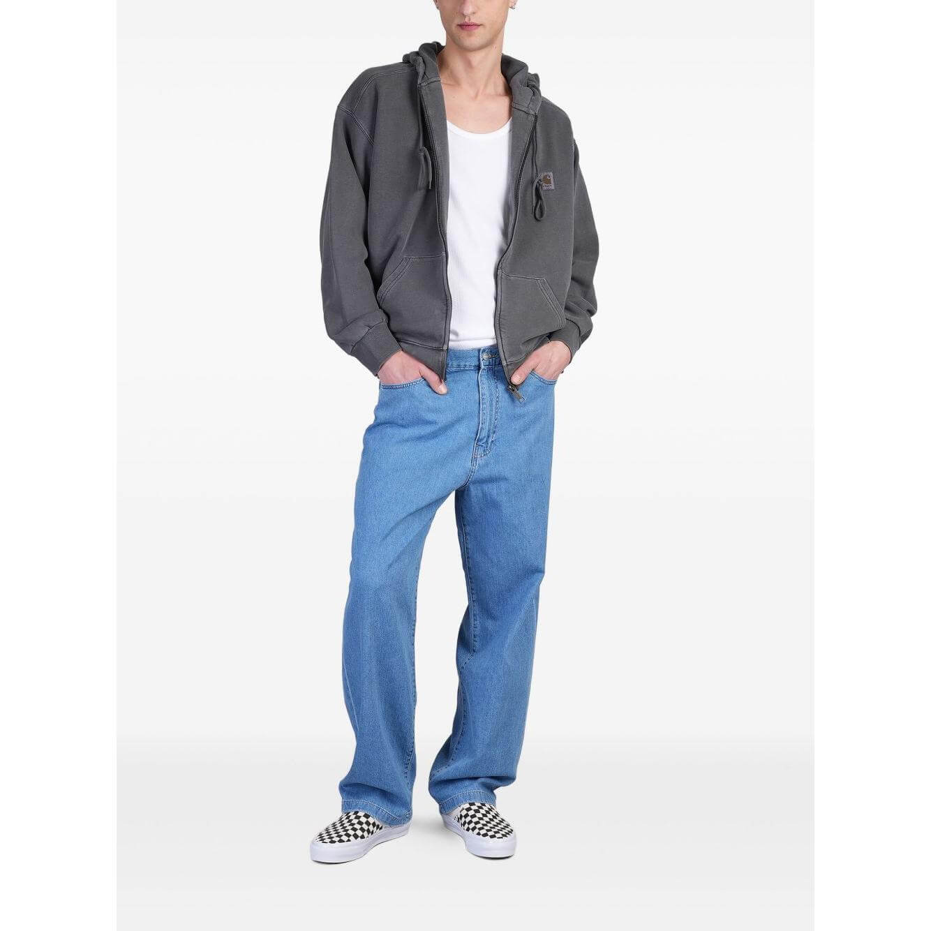 Model wearing CARHARTT WIP MAIN grey hoodie with zip fastening, drawstring hood, and patch pockets, paired with blue jeans and checkered sneakers.