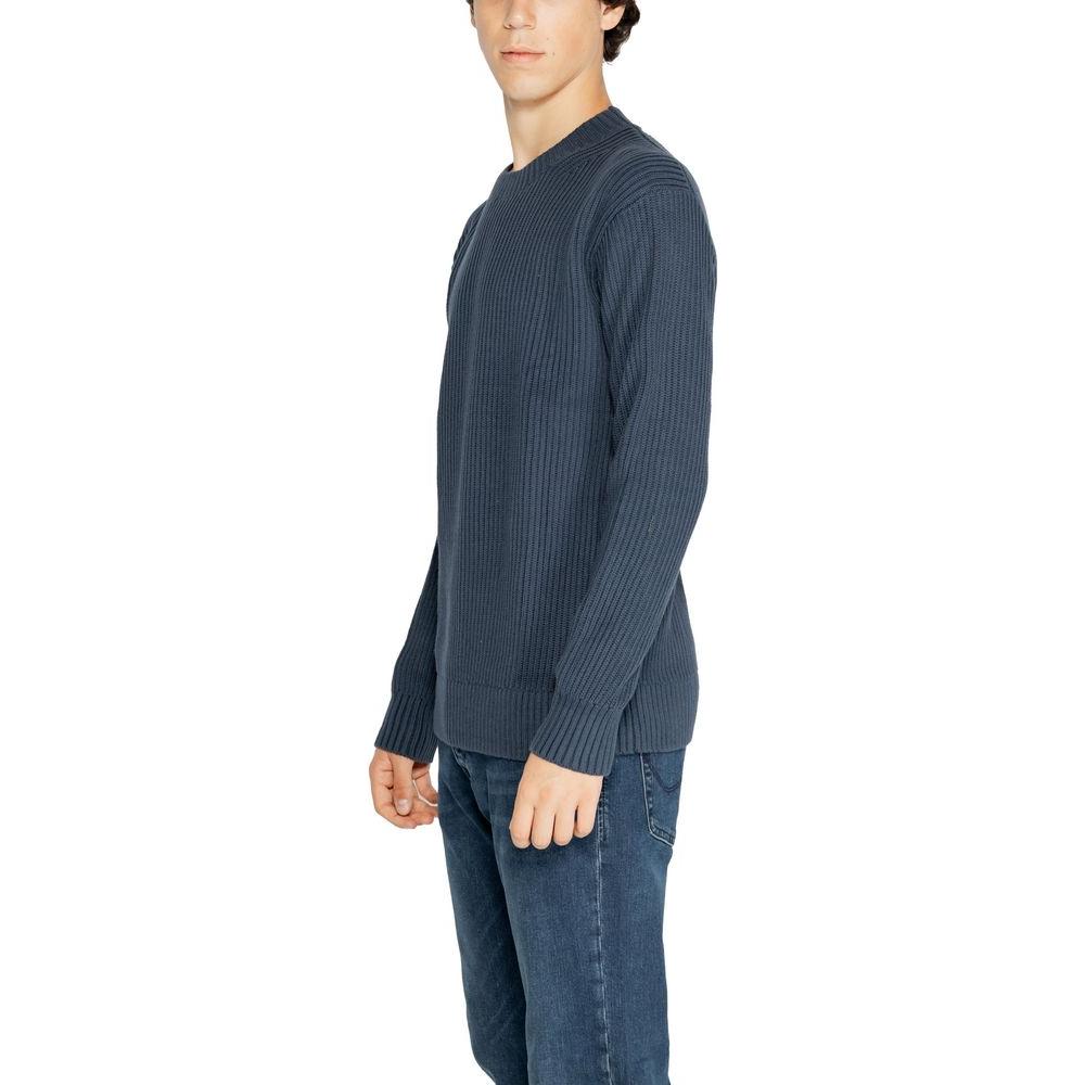Model wearing Calvin Klein black organic cotton knit sweater, part of men's fall/winter collection, with blue jeans, side view.