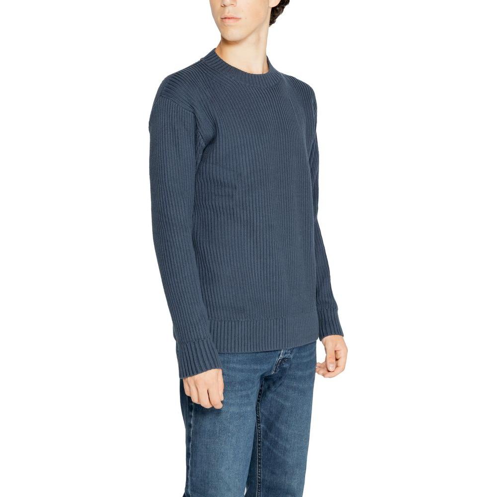 Man wearing a blue knit sweater with ribbed texture and blue jeans, showcasing fall/winter casual men's fashion.