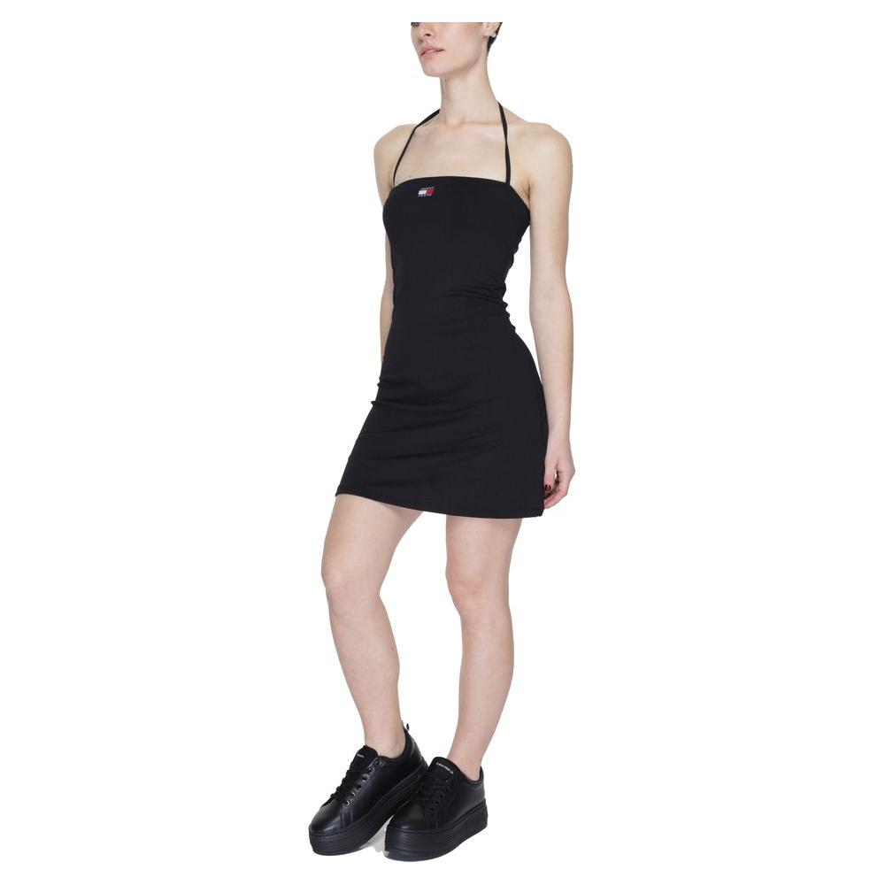 Woman wearing Tommy Hilfiger black recycled polyester dress, short style, spring/summer collection, paired with black sneakers.