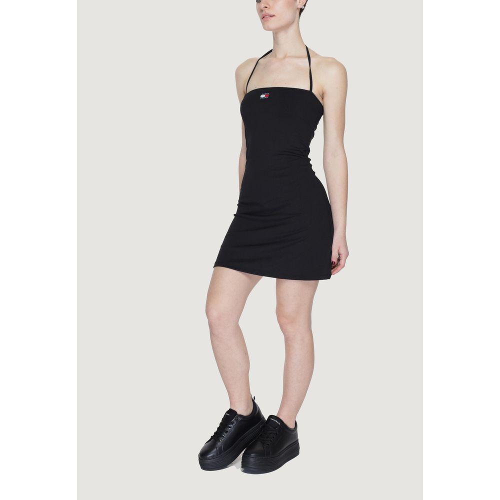 Woman wearing Tommy Hilfiger black recycled polyester dress, spring/summer collection, front view, standing pose with black sneakers.