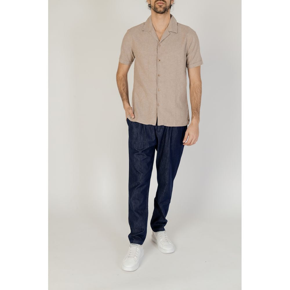 Men's beige short-sleeved linen shirt by Hamaki-Ho, spring/summer collection, paired with dark jeans and white sneakers.