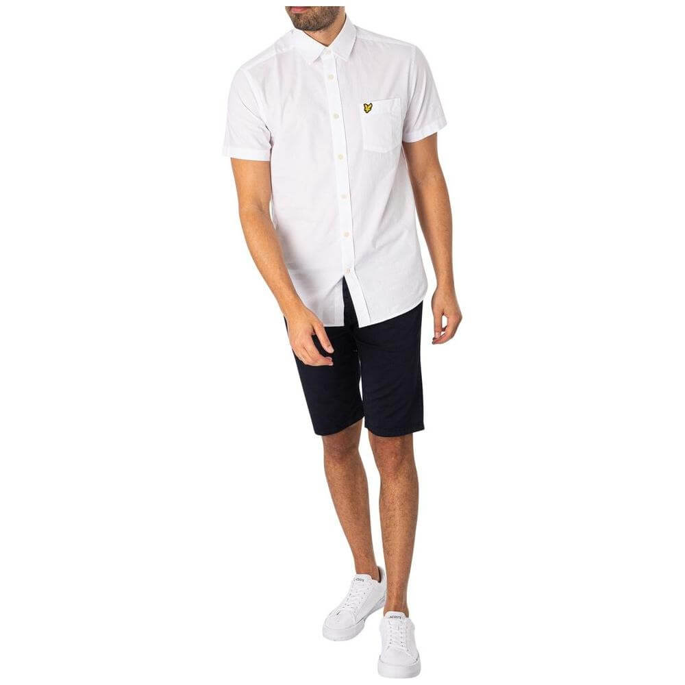 Man wearing Lyle & Scott blue cotton shorts and white shirt, showcasing men's fall/winter fashion ensemble with casual style.