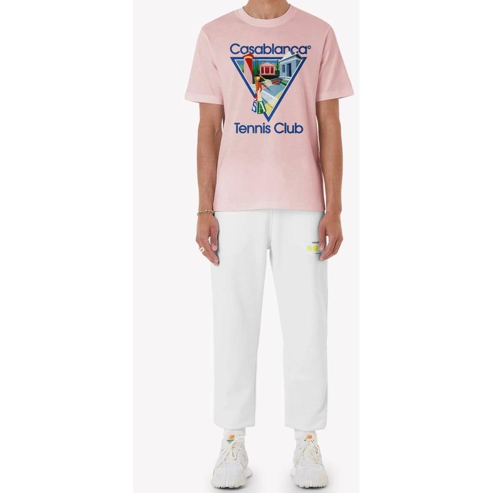 Man wearing a pale pink Casablanca 100% cotton crew-neck t-shirt with tennis club print, paired with white pants and sneakers.
