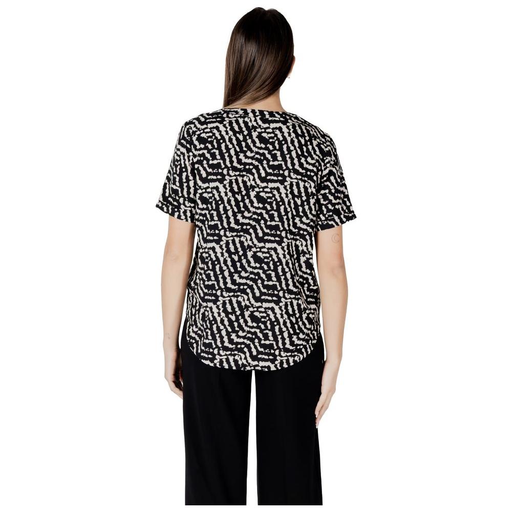 Back view of woman wearing black and white patterned short-sleeve Street One viscose shirt with turn-up sleeves and black trousers.